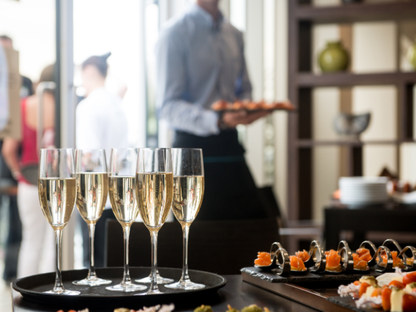 a table of champagne, in the background a waiter walks through a party with a tray